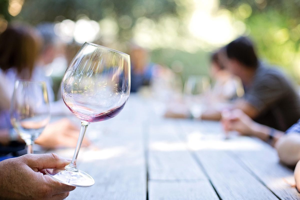 Un verre de vin rouge tenu à la main lors d'un repas en plein air, autres convives flous en arrière-plan Un verre de vin rouge tenu à la main lors d'un repas en plein air, autres convives flous en arrière-plan