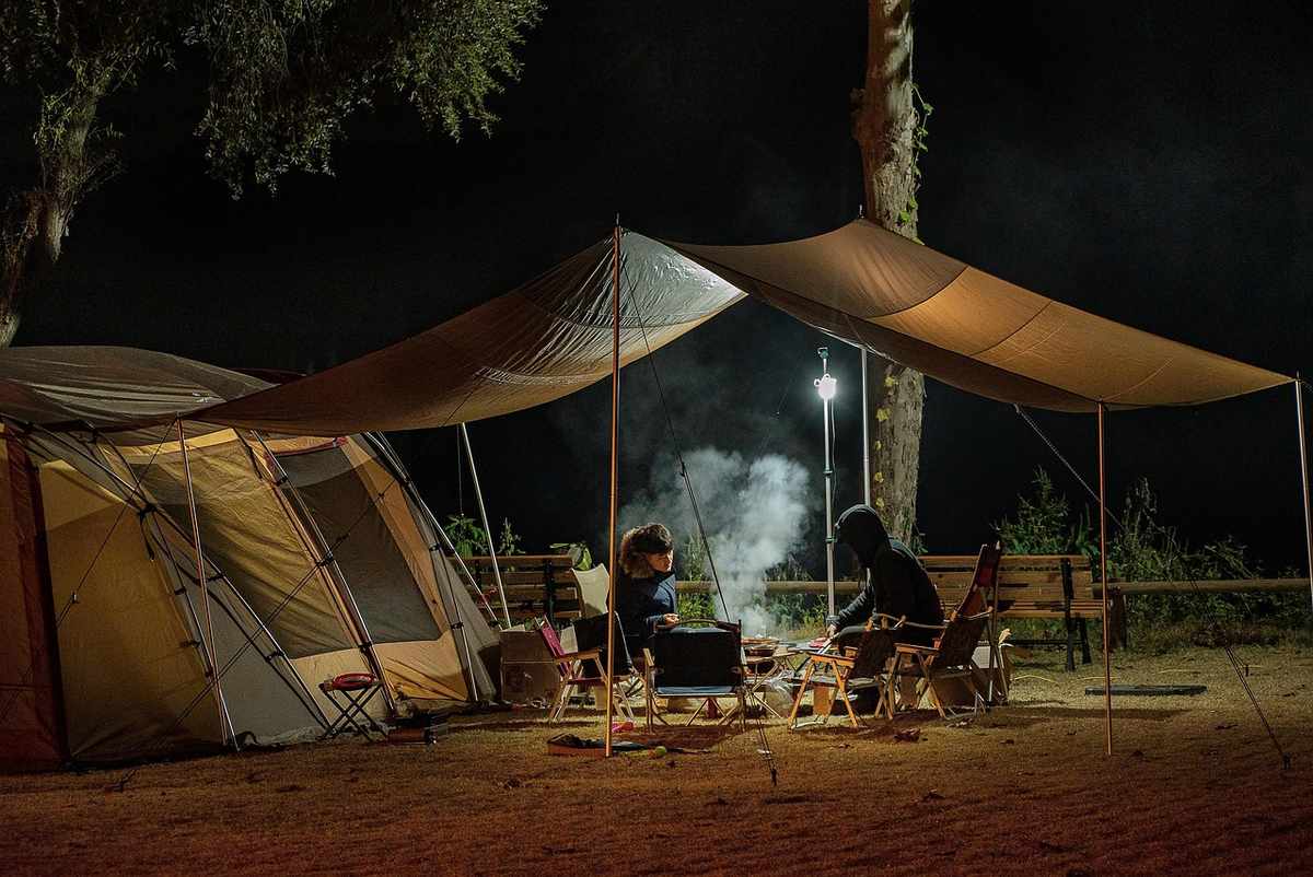 Campement de nuit avec tentes aménagées, feu de camp allumé et visiteurs assis autour Campement de nuit avec tentes aménagées, feu de camp allumé et visiteurs assis autour