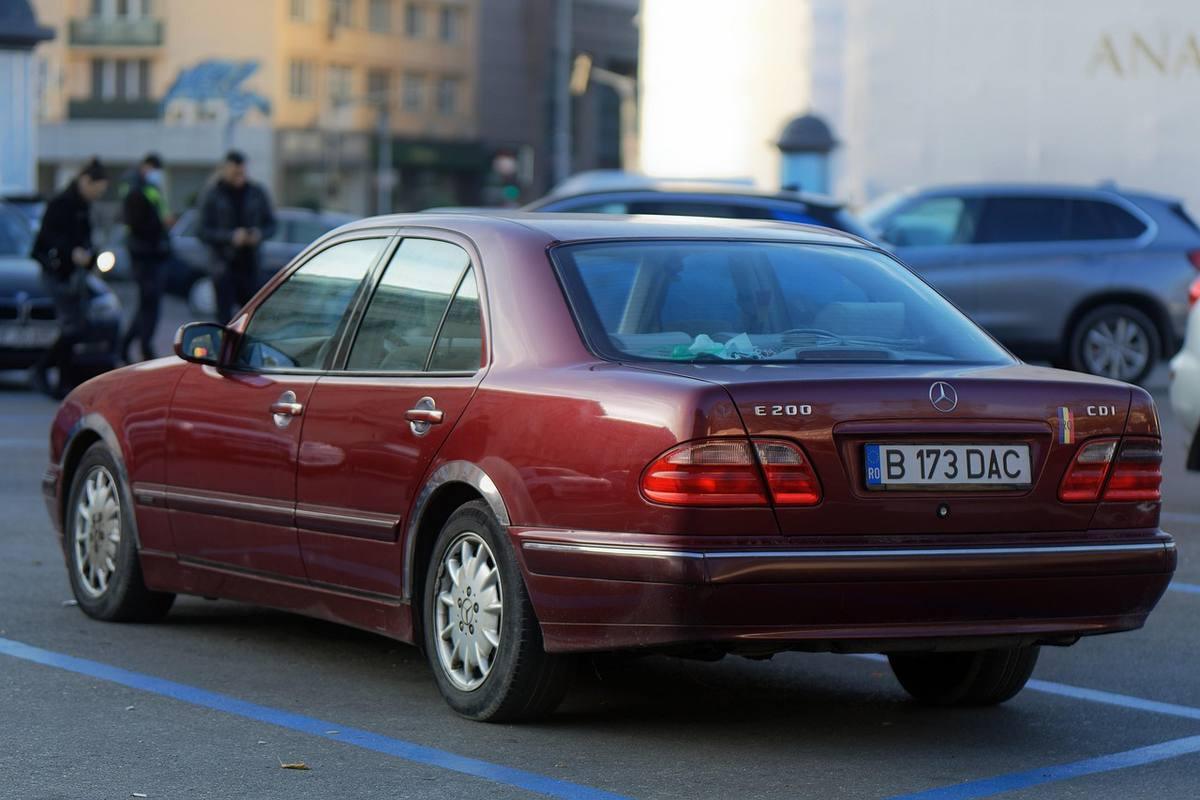 Mercedes berline rouge garée sur un parking urbain avec immeubles en arrière-plan Mercedes berline rouge garée sur un parking urbain avec immeubles en arrière-plan