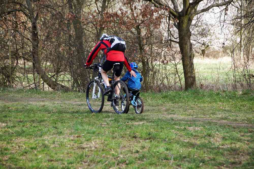 Un adulte aide un enfant à pédaler sur un vélo dans la forêt Un adulte aide un enfant à pédaler sur un vélo dans la forêt